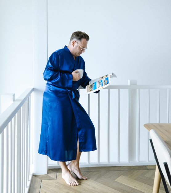 Man in blauwe satijnen kimono met kop koffie magazine lezen