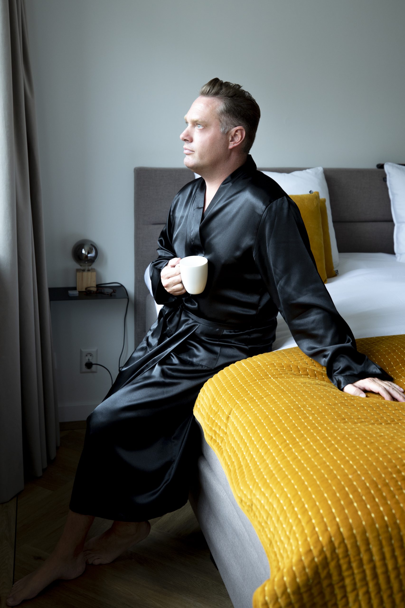 Man in satijnen kimono op bed met kop koffie
