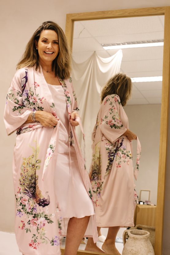 Vrouw in satijnen roze kimono met pauw voor de speigel